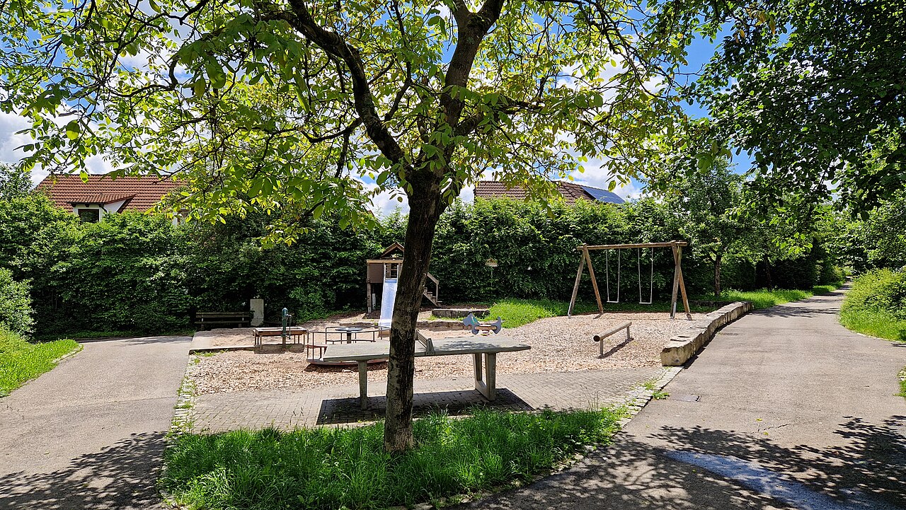 Spielplatz mit verschiedenen Spielgeräten bei Sonnenschein und weißen Wolken am Himmel