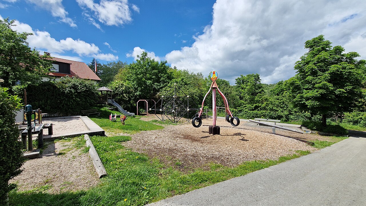 Spielplatz mit verschiedenen Spielgeräten bei Sonnenschein und weißen Wolken am Himmel
