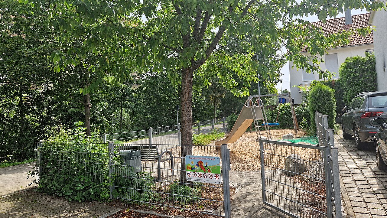 Kleiner Spielplatz mit verschiedenen Spielgeräten bei Sonnenschein und weißen Schleierwolken am Himmel